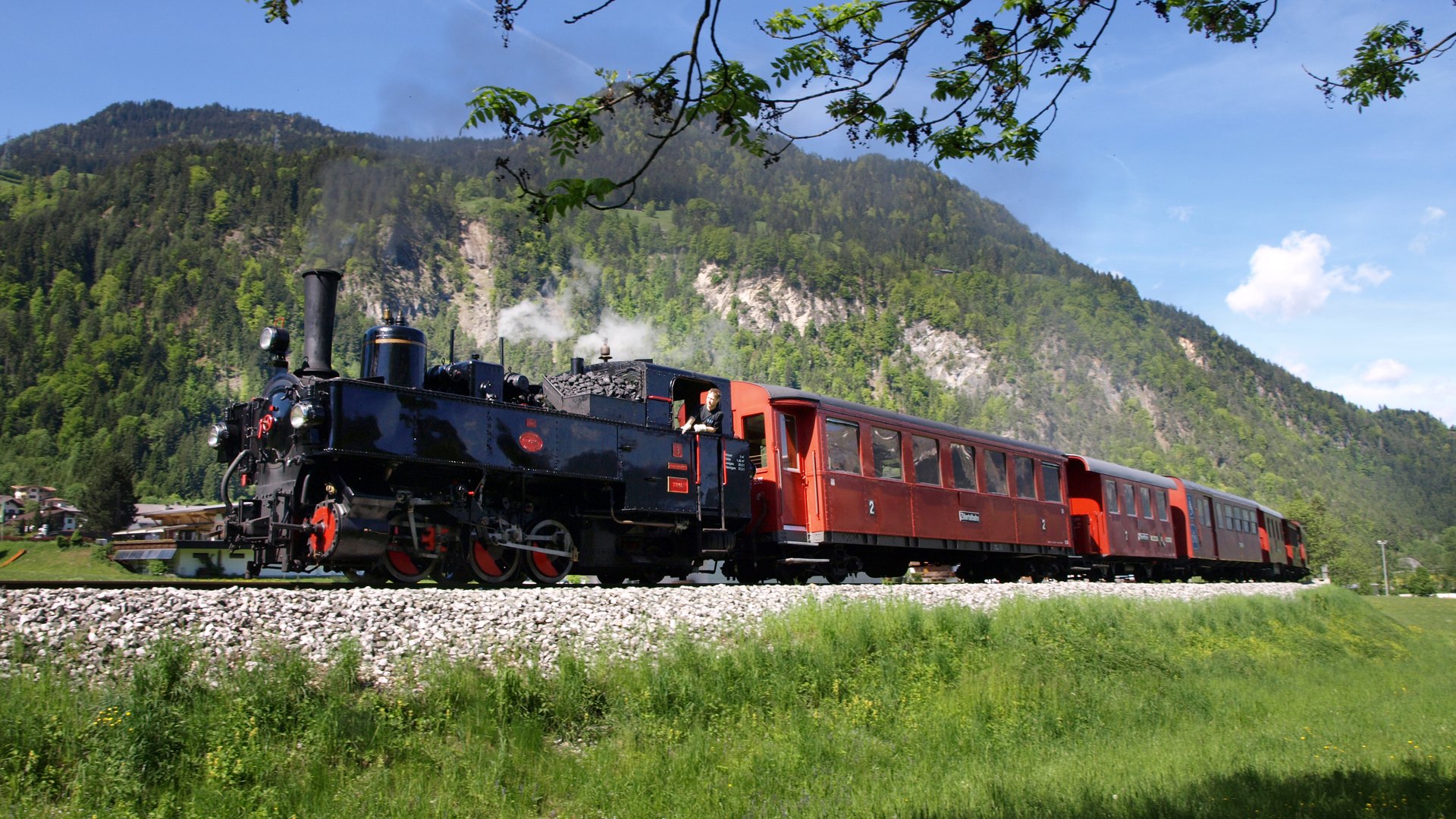 Dampfzug der Zillertalbahn mit roten Wagen auf der Strecke bei Schlitters